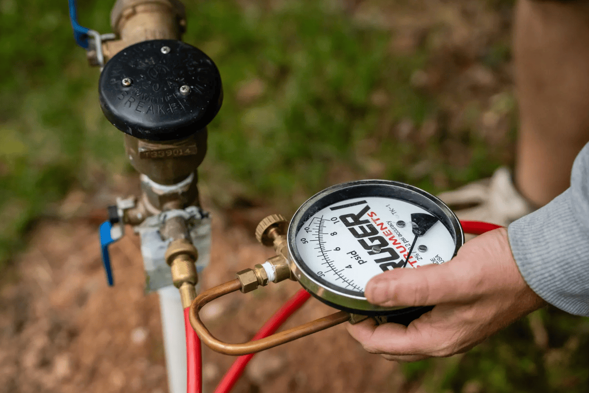 Hand checking water pressure gauge on pipe